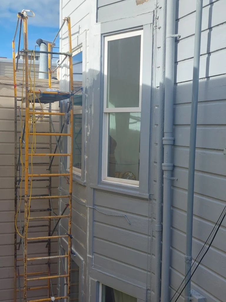 Scaffolding stands next to a recently painted building, highlighting ongoing exterior renovation. A new window is visible, indicating updates to the property.