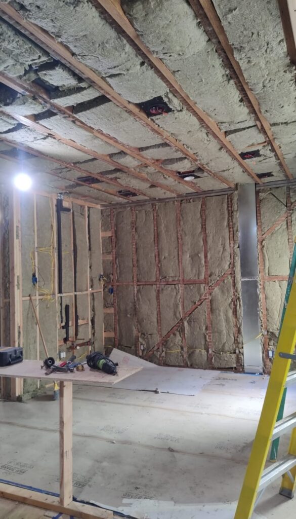 Renovation progress showcasing a partially constructed room with insulated walls and ceiling, tools on a worktable, and a ladder.