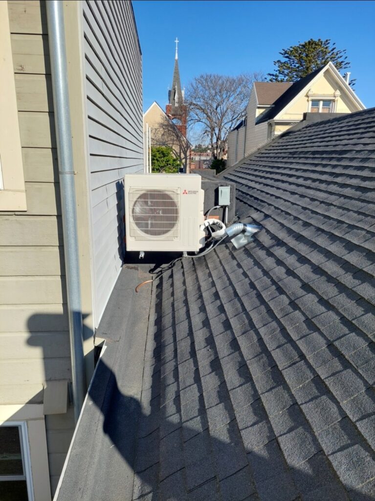 Outdoor HVAC unit mounted on a roof, with a church steeple visible in the background. The clear sky indicates good weather.