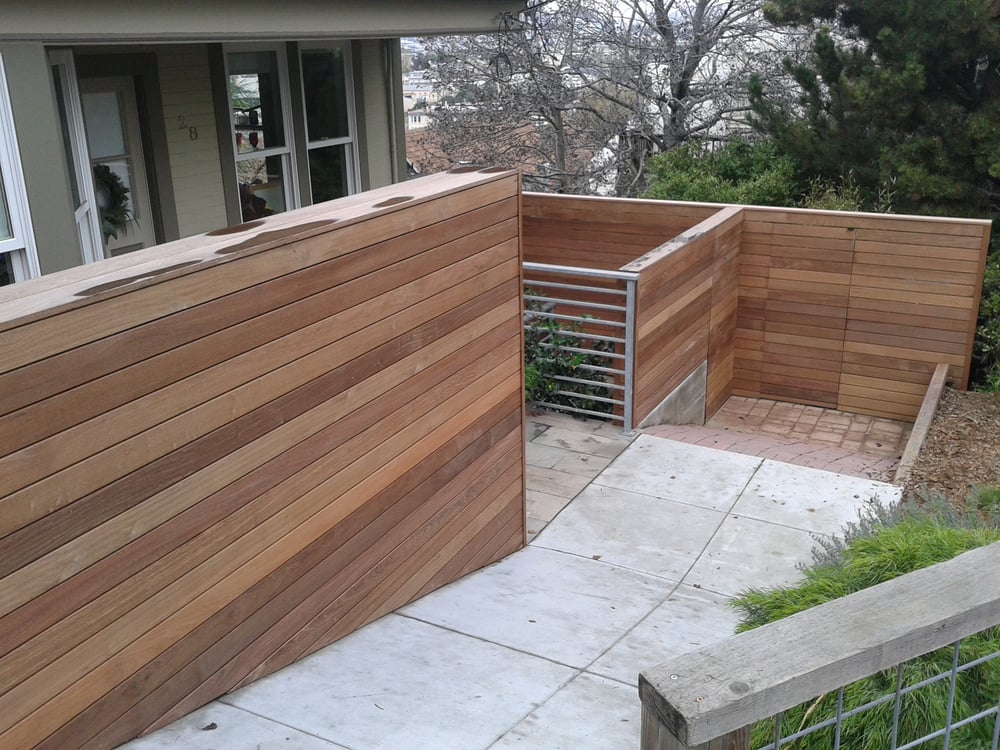 Wooden fencing and a modern railing outline a landscaped pathway leading to a home entrance, showcasing contemporary outdoor design.