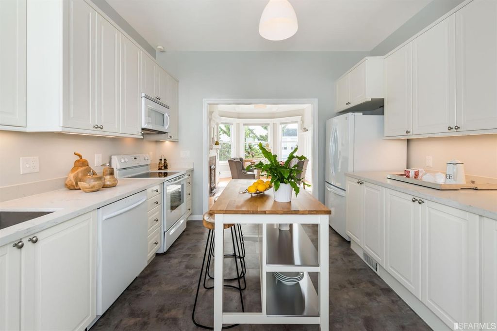 Bright, modern kitchen featuring white cabinets, stainless steel appliances, and a central wooden island with fresh fruit, creating an inviting atmosphere.