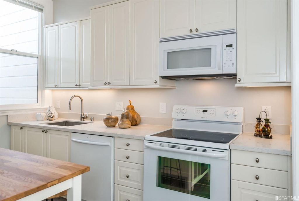 Modern kitchen featuring light cabinetry, quartz countertops, stainless steel appliances, and a window providing natural light.