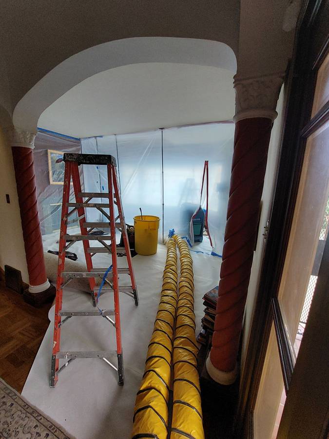 Construction scene showing a ladder, yellow ventilation hose, and plastic sheeting. This image illustrates ongoing home renovation work.