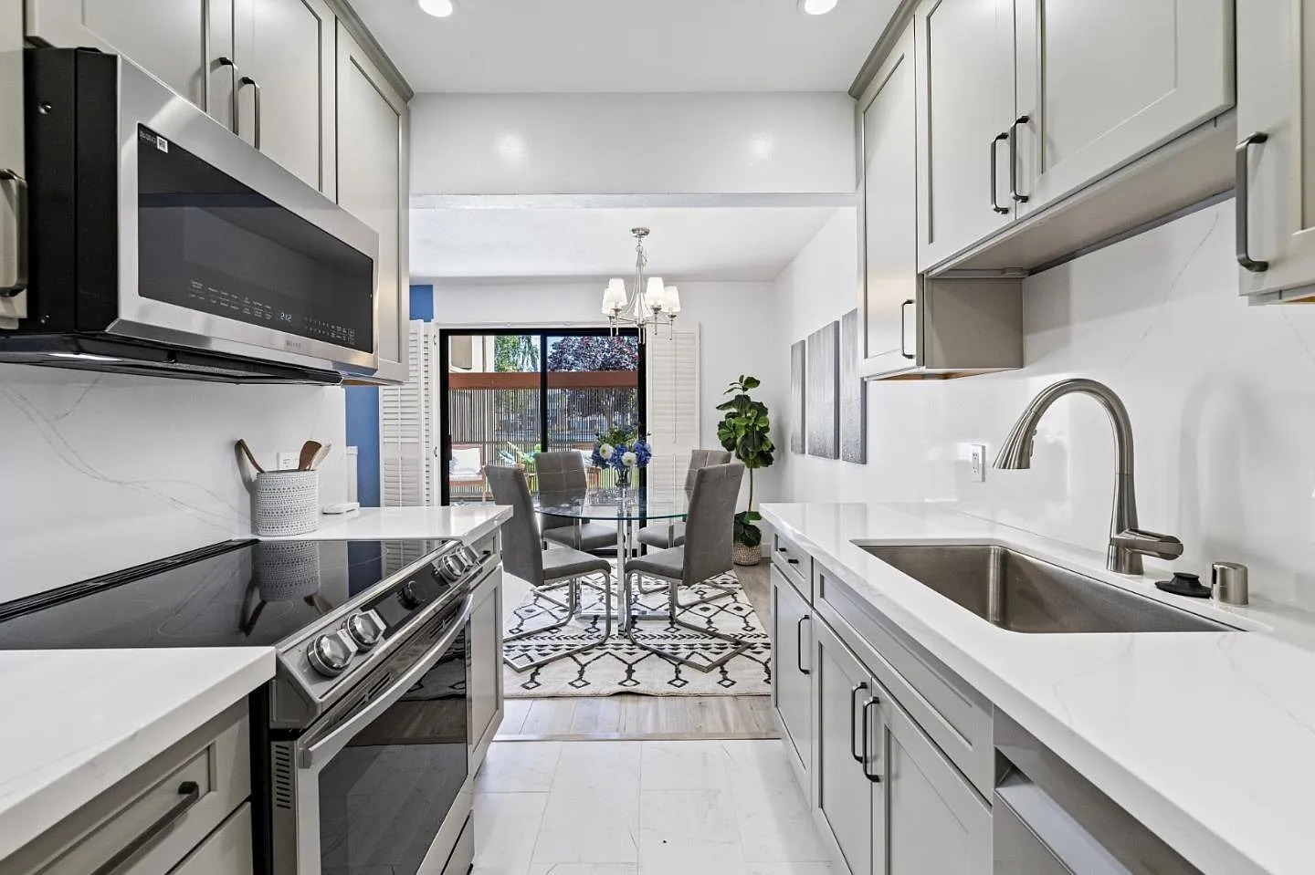 Modern kitchen featuring stainless steel appliances, sleek cabinetry, and a dining area with a glass table, overlooking a patio garden.