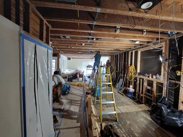 Renovation in progress with a worker on a ladder installing lights. Exposed beams and tools are visible, showcasing an active construction site.